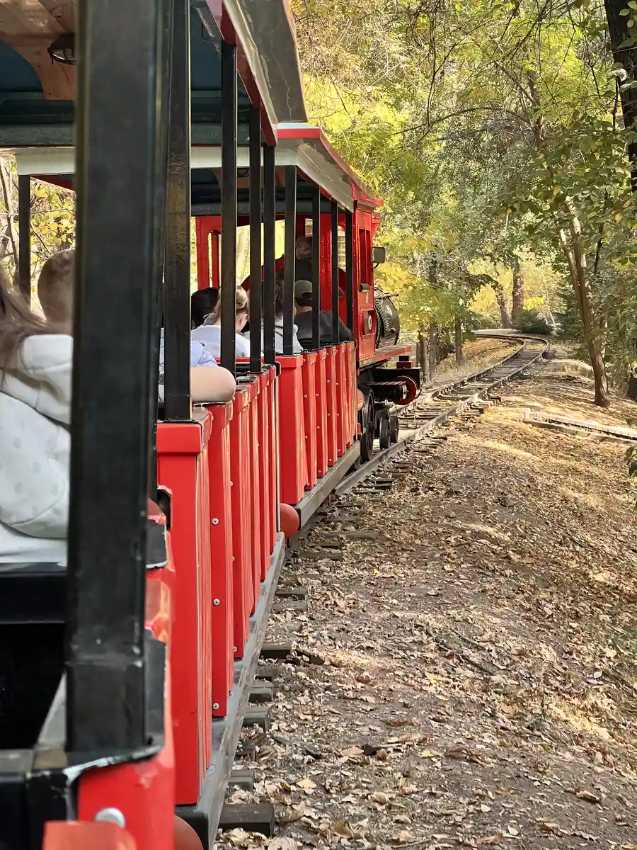Passengers riding a small red tourist train through the autumn trees of Gorky Park in Almaty
